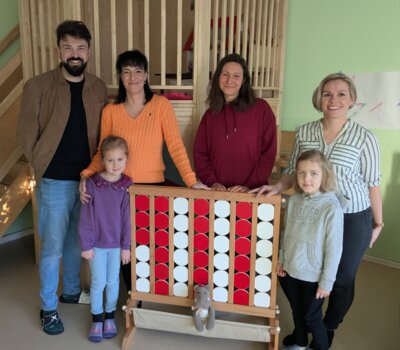 Die Kita-Leitung und Stellvertreter:in nehmen unter den wachsamen Augen der Kinder das gespendete ‚Vier gewinnt‘-Spiel von Ulrike Lichtnow in Empfang.