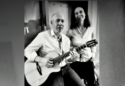 Das Schwarz-Weiß-Foto zeigt Henning und Wibke Knapheide. Beide sehen freundlich in die Kamera und Henning Knapheide spielt auf seiner Gitarre.