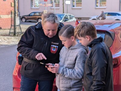 Andrea Noack, Mitarbeiter des Ordnungsamtes, zeigt Emil Giedow (Mitte) und Lucas Jerome Weise wie ein "Knöllchen" ausgedruckt wird. Foto: Stadt Calau / Jan Hornhauer (Bild vergrößern)