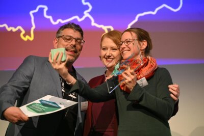 Felix Römer (li., Künstl. Leiter für die Bewerbungsphase Aller.Land für den WMK, zusammen mit Anna Barth (re., Projektmitarbeiterin “Eine gute Stunde für den WMK“ bei der Preisübergabe durch Bundesseniorenministerin Lisa Paus). (Bild vergrößern)