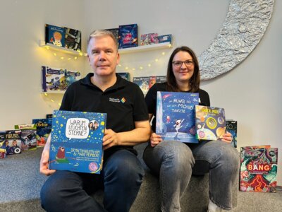 Mayk Plewka von den Stadtwerken Wittenberge und Bibliotheksmitarbeiterin Johanna Gumz zeigen neue Bücher und Medien, die für den diesjährigen Mediensommer angeschafft wurden I Foto: Martin Ferch (Bild vergrößern)