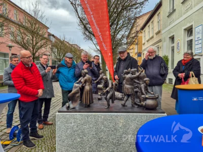 Künstler Bernd Streiter (hinten Mitte) erklärt die einzelnen Figuren in der Skulptur im „Talerreigen“ der Volks- und Raiffeisenbank. Foto: Stadt Pritzwalk (Bild vergr&ouml;&szlig;ern)