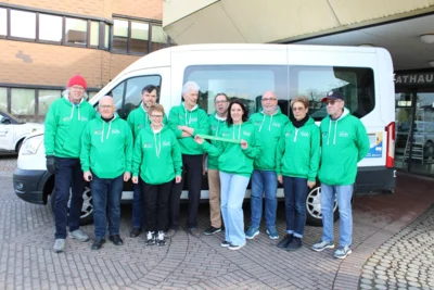 Vor dem Rathaus Mandelbachtal bringt das Team des Bürgerbusses das grüne Band am Fahrzeug an (v. l.): Tom Manley, Wolfgang Dinger, Reinhold Ernst, Marlene Groh, Erwin Niederländer, Franz Schmidt, Kerstin Bauer mit dem grünen Solidaritätsband, Josef Bauer, Karin Hofmann und Harald Karcher. Foto: Stefan Eins, Gemeinde Mandelbachtal