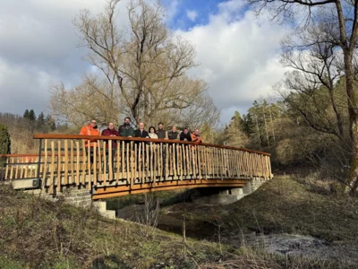 Nach langer Bauzeit nun offiziell ihrer Bestimmung übergeben: mit der neuen Brücke über den Aselbach gelangt man nun wieder zum Nationalpark-Eingang Strieder Eiche  Auf der Brücke v.l.n.r. freuen sich:  Axel Sobirey (WAGU - Gesellschaft für Wasserwirtschaft, Gewässerökologie und Umweltplanung mbH) (Planung Umwelt+Ökologie, örtliche Bauüberwachung), Michael Krieg (Kammerdiener Krieg Baugesellschaft mbH) (Generalunternehmer), Johannes Flikschuh (ehem. HessenForst Technik) (Bauherr), Karsten Kalhöfer (Bürgermeister Gemeinde Vöhl), Angela Bauer, Manuel Schweiger, Achim Frede (Nationalpark Kellerwald-Edersee) (Baulastträger), Thomas Ruch (Ortsbeirat Asel), Frank Miebach (Ingenieurbüro Miebach) (Gesamtplanung, Bauoberleitung)  Nicht auf dem Bild: Schmees & Lühn GmbH & Co. KG (Holz- und Stahlbau) Elementbau Osthessen GmbH & Co., ELO KG (Betonfertigteilbau)   Bildautor: Inka Lücke/ Nationalpark Kellerwald-Edersee (Bild vergr&ouml;&szlig;ern)