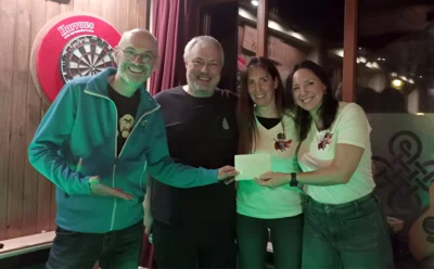Foto: Auf dem Foto sind von links zu sehen: Bernd Dörsam, Michael Böhler, Heike Klemm und Christina Luhn. Sie alle schauen lachend in die Kamera. Bernd Dörsam übergibt gerade den Spendenumschlag an Christina Luhn. Foto zur Meldung: Odenwälder Abend im Mac Menhir – voller Erfolg für den guten Zweck!