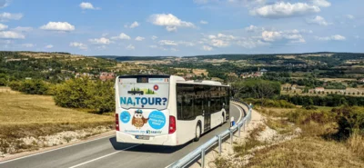 Bus des Saarländischen Verkehrsverbunds auf einer kurvigen Landstraße im Bliesgau oberhalb von Reinheim mit Blick über die Hügellandschaft und zu den Dörfern im Bliestal. Auf der Rückseite des Busses steht „NA, TOUR?“. Foto: Maurice Eickhoff, Mobilitätsmanager des Saarpfalz-Kreises.