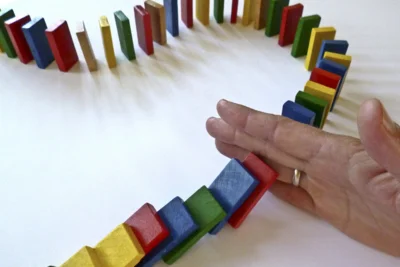 Symbolbild: Unterbrechung - Hand stoppt bunte Dominosteine - Christine Schmidt, Pixabay