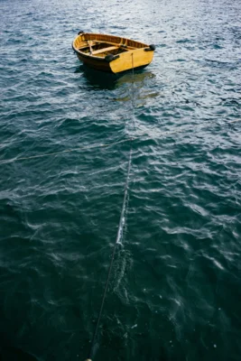 Ein leeres Boot, dass an einem langen Tau auf dem Wasser schaukelt. Das Tau kommt aus dem Wasser, man kann nicht erkennen, wo es befestigt ist. (Bild vergr&ouml;&szlig;ern)