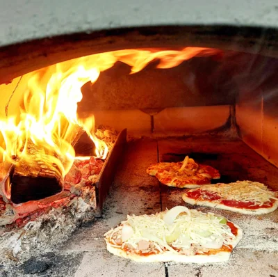 3 Pizzen backen in einem großen Ofen, Links sind Flammen zu sehen. (Bild vergr&ouml;&szlig;ern)