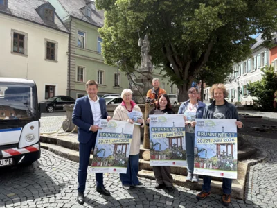 Bildunterschrift: Erster Bürgermeister Nicolas Lahovnik präsentiert gemeinsam mit den verantwortlichen Akteuren aus dem Rathaus und den Forstbetrieben sowie dem JuKu- Mobil Fichtelgebirge & Hofer Land das Programm zum Brunnenfest vor dem diesjährigen Jubiläumsbrunnen (v.l.n.r.): Erster Bürgermeister Nicolas Lahovnik, Angelika Groß (Ordnungsamt), Markus Roßmeisl (Forstbetrieb), Eva Theresa Beck (Leiterin Kultur- und Tourismusmarketing), Petra Sommerer (Tourist-Info), Stefan Frank (Geschäftsführer JuKu Mobil Fichtelgebirge & Hofer Land)
