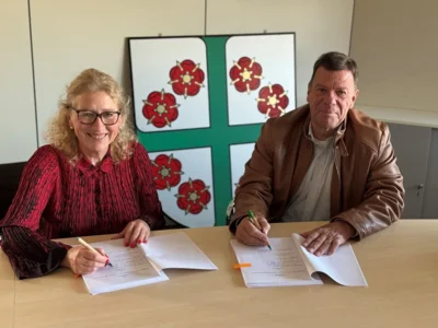 Bürgermeisterin Maria Vermeulen und Investor Clemens Dahlem unterzeichnen den städtebaulichen Vertrag zum Bebauungsplan „Gewerbegebiet Nördlich Adenauer Straße“. Im Hintergrund ist das Wappen der Gemeinde Mandelbachtal zu sehen.