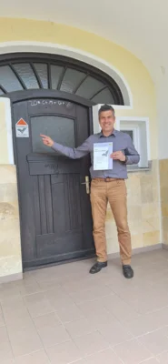 Bürgermeister Ben Matthes vor der „Alten Schule“ in Wörleschwang. Die Plakette weißt auf die Wochenstube des Großen Mausohrs im Dachboden des Gebäudes hin. (Bild vergr&ouml;&szlig;ern)