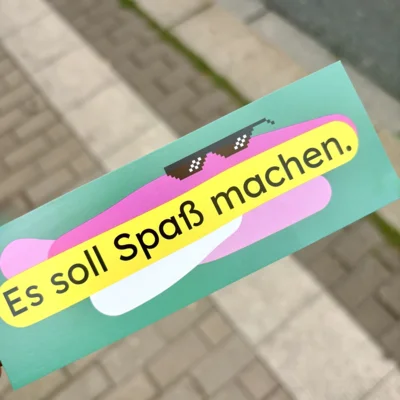 Im Vordergrund das Lesezeichen, darauf steht: Es soll Spaß machen. Im Hintergrund: eine Straße. (Bild vergr&ouml;&szlig;ern)