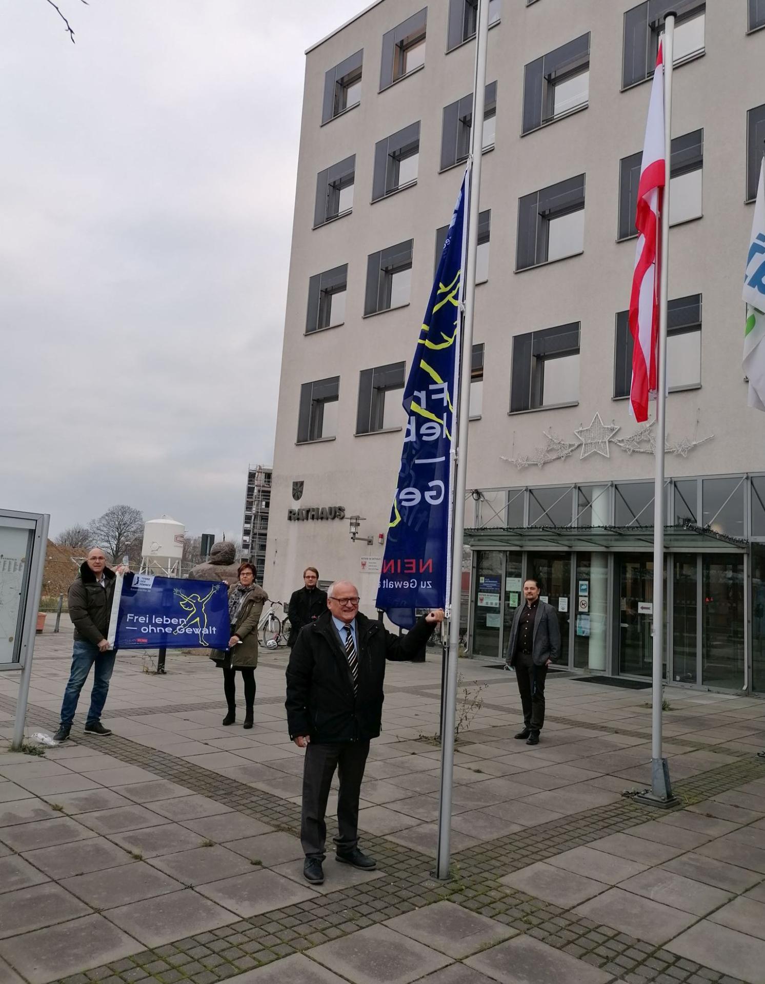 Schönefeld: Bürgermeister Christian Henschel (vorn) hisst gemeinsam mit weiteren Mitarbeitern die Flagge, zusätzlich wird ein Banner gezeigt. Foto: Gemeinde Schönefeld