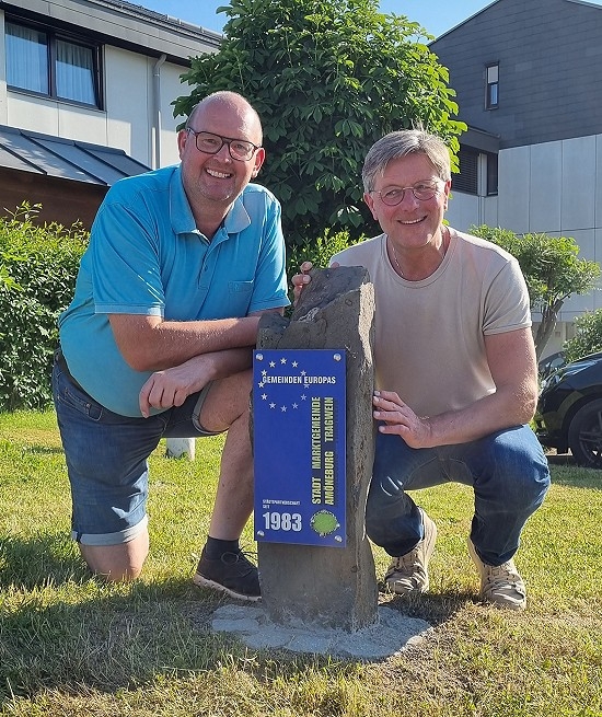 zwei Männer hocken vor einem Stein mit einem Schild Gemeinde Europas
