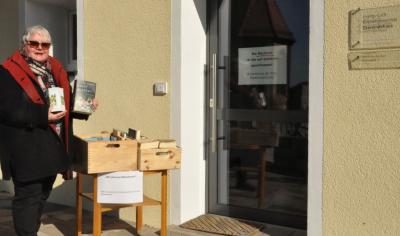Angelika Fiederling von der evangelischen Gemeindebücherei Puschendorf präsentiert den rund um die Uhr geöffneten Freiluft-Büchertisch  vor dem geschlossenen Gemeindehaus für alle Leseratten, denen der Lesestoff ausgegangen ist.
