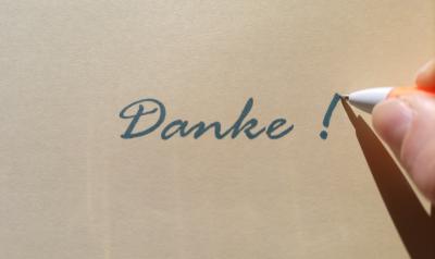Das Bild zeigt rechts noch einen Teil einer Hand, die einen Kugelschreiber hälst, der soeben ein Ausrufezeichen hinter dem Wort Danke fertig schreibt.
