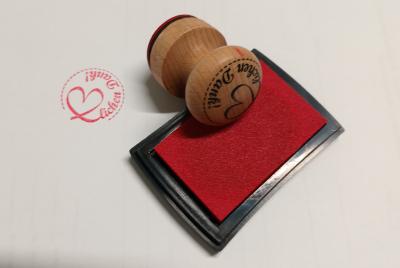 Auf dem Bild sieht man einen Stempel auf einem Stempelkissen mit roter Farbe liegen, mit dem soeben Herzlichen Dank auf ein Blatt Papier gestempelt wurde. Das Wort Herz im Schriftzug ist in Form eines Herzens dargestellt.