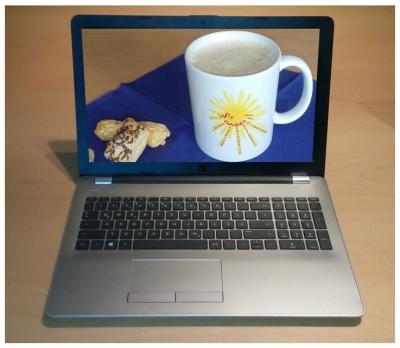 Auf dem Foto sieht man ein aufgeklapptes Notebook und auf dessen Display eine Kaffeetasse mit dem Wir DABEI!-Logo welche mit zwei kleinen Blätterteigteilchen auf einer blauen Serviette steht.
