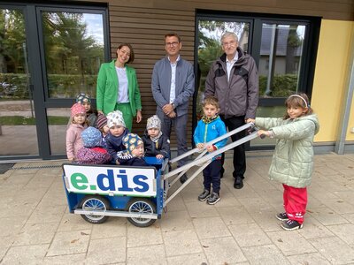 Unser Bild zeigt Wiebke Schneider, Lars Klemmer, Bürgermeister Heiko Müller und die Kinder mit dem neuen Kleinkinderwagen vor dem Kitagebäude im Rohrbecker Weg.