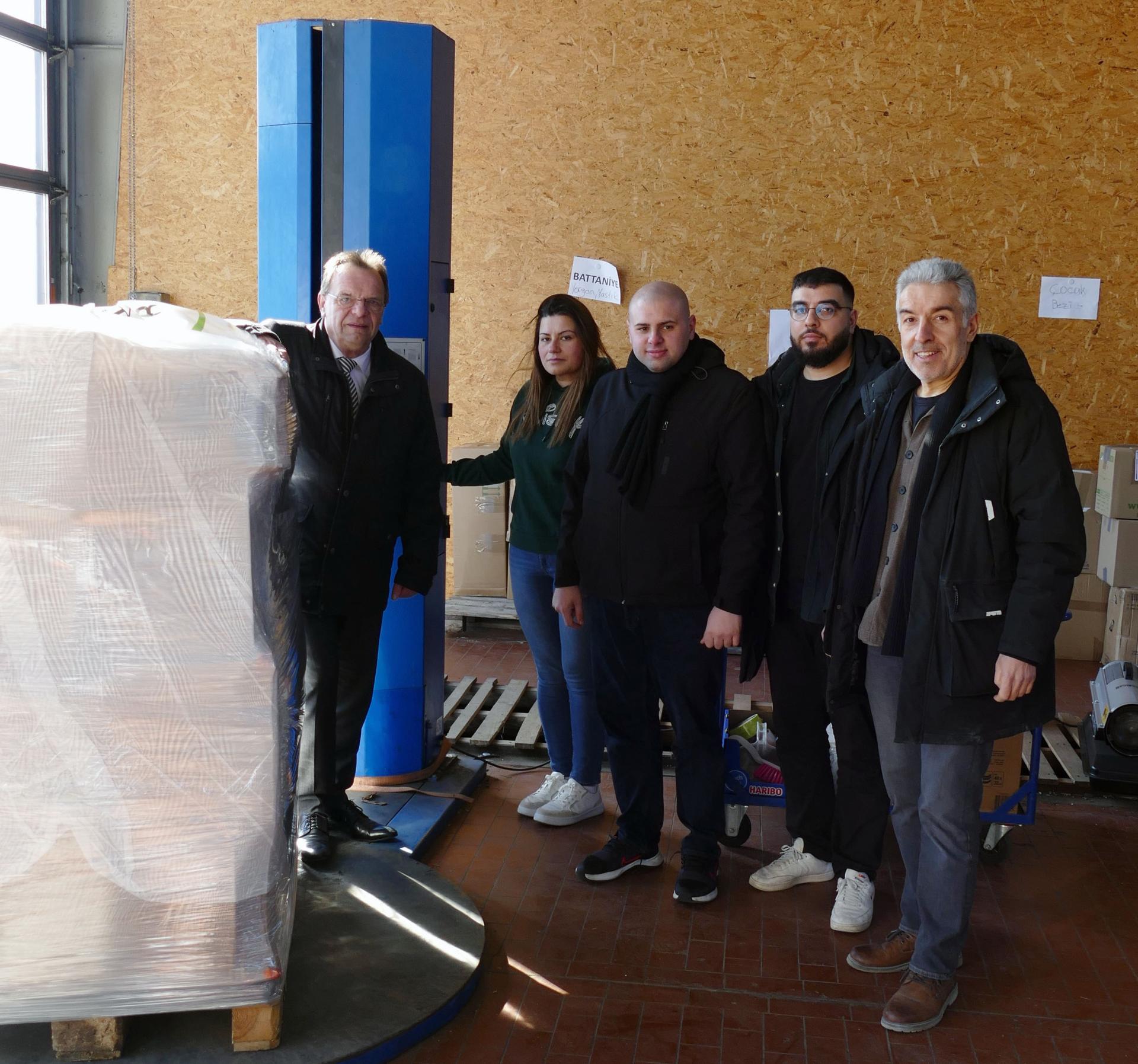 Bildunterschrift: An der Verpackungsmaschine, um gespendete Hilfsgüter sicher auf Paletten für den Transport per LKW vorzubereiten: (v. li.) Landrat Winfried Becker ließ sich von Nurcan Inan, Gökhan Mete, Ihsan Cetinkaya und Murat Cetinkaya von der Erdbebenhilfe Kassel vor Ort zeigen, wie die Hilfsgüter verpackt werden, um sie in das Erdbebengebiet zu bringen. (Bildautor: Stephan Bürger | Kreisverwaltung Schwalm-Eder)