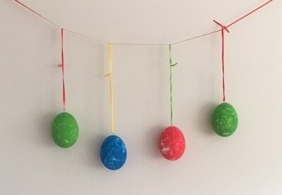 Auf dem Bild sind vier Eier die grün, blau und rot angemalt und an bunten Bändern aufgehängt sind zu sehen.
