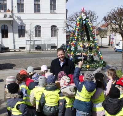 Osterbrunnen Marktplatz - Bürgermeister Sebastian Busse steht vor dem Brunnen umringt von Kindern der Kita Rhinstrolche