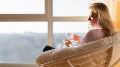 Frau sitzt am Fenster mit einer Tasse Tee und denkt über die Wechseljahre nach (Bild vergr&ouml;&szlig;ern)
