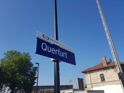 Bahnhofsschild mit der Aufschrift Querfurt darüber ein Werbeschild für Mein Takt