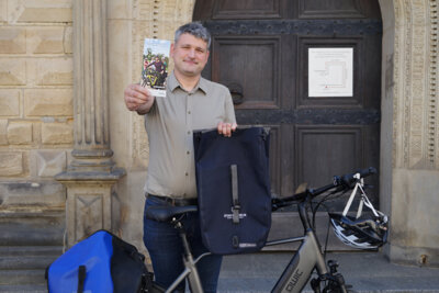 Der Klimaschutzbeauftragte der Stadt, Dr. André Wüste, zeigt einen Flyer und einen der Preise, eine hochwertige Fahrradtasche. (Bild vergrößern)