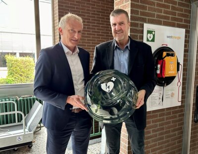 Bildunterschrift: Erster Beigeordneter Bernd Kasischke (r.) und Dirk Wißel, Kommunalmanager bei Westenergie (l.), bei der Übergabe des Defibrillators an das Schulzentrum an der Opherdicker Straße. Foto: Katrin Frendo / Westenergie AG