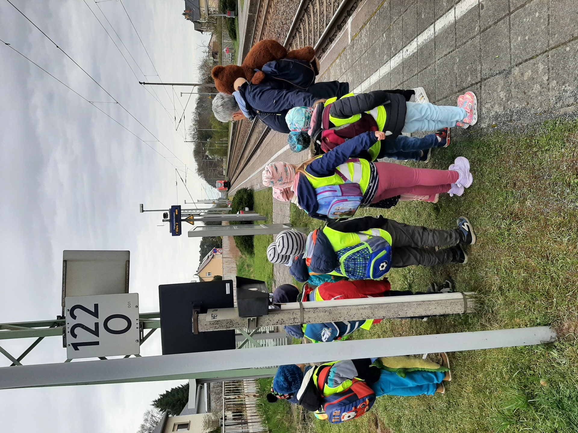 Kinder am Bahnsteig mit gelben Warnwesten, einfahrender Regionalzug