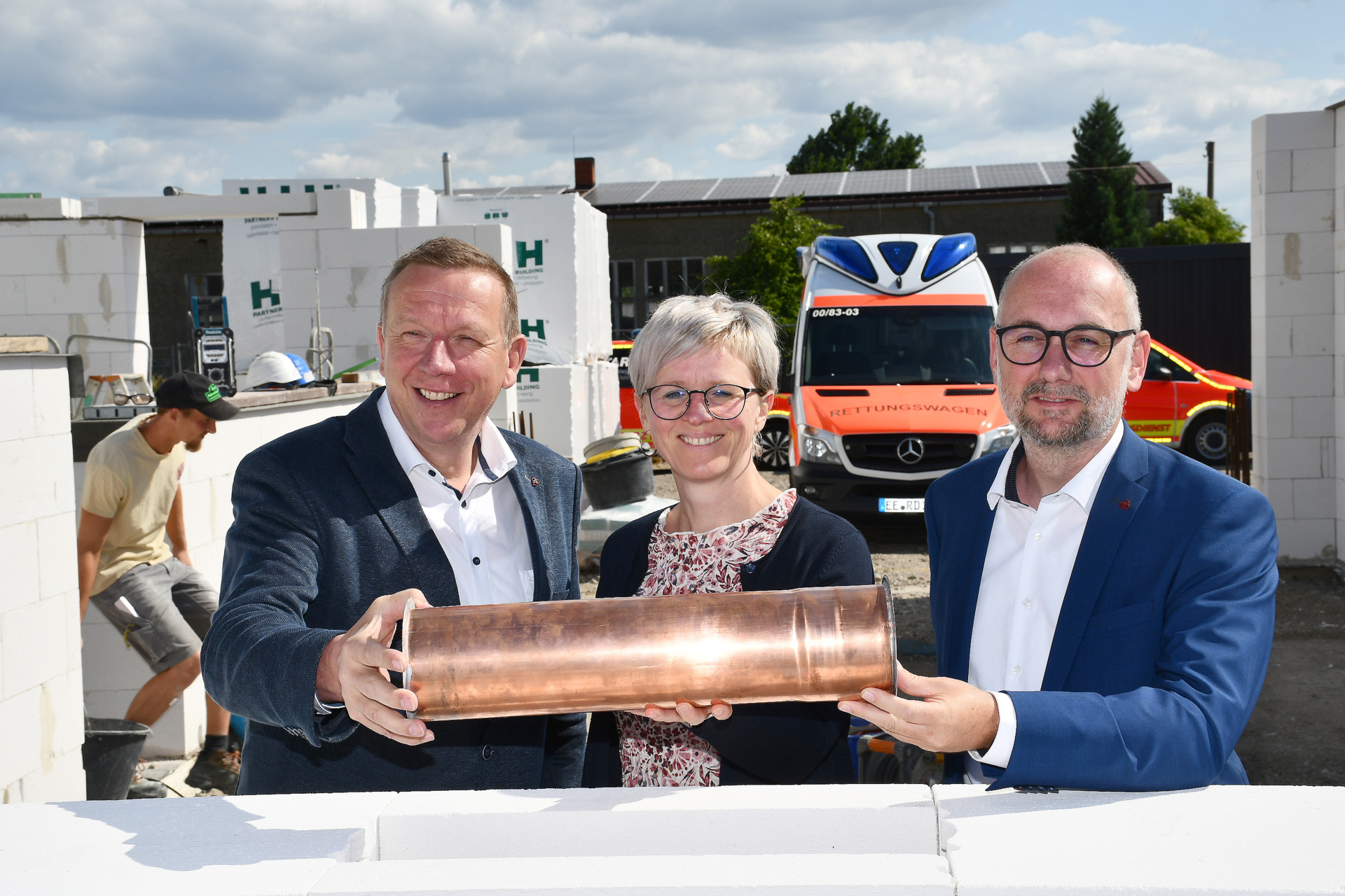 Feierlicher Moment in Großthiemig: Landrat Christian Jaschinski, Amtsdirektorin Kathleen Wilken und Werkleiter Sebastian Weiss (v.l.n.r.) versenken gemeinsam eine kupferne Zeitkapsel im Grundstein der neuen Rettungswache – ein Zeichen für Zukunft und Engagement im Rettungsdienst.