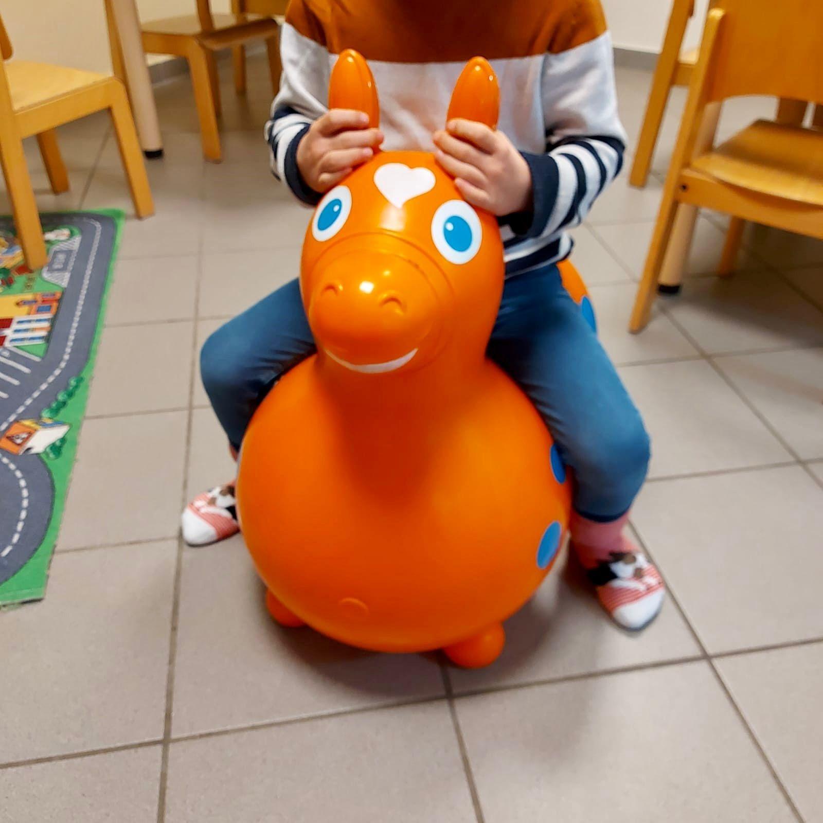 Auf dem Foto sieht man ein Kind, das auf einem roten Gummi-Hüpfpferd sitzt. Der Kopf des Kindes ist auf dem Bild nicht zu sehen.
