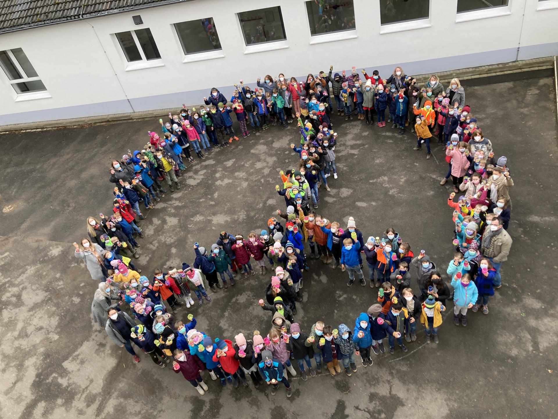 Kinder bilden das PEACE Symbol auf dem Schulhof