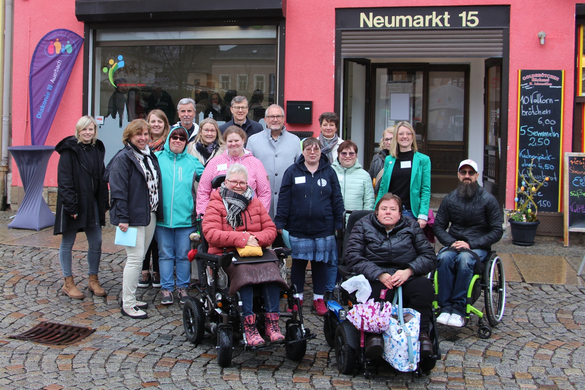 Auf dem Bild sind mehrere Menschen vor dem Büro zur Eröffnung zu sehen. Drei sitzen im Rollstuhl. Alle lächeln in die Kamera.