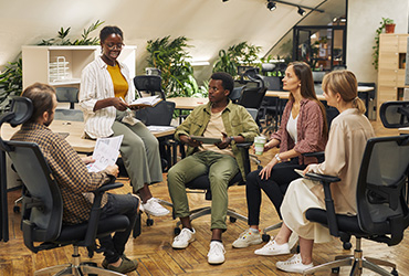 full-length-portrait-multi-ethnic-group-young-people-discussing-work-project-while-sitting-circle-modern-office-listening-female-manager