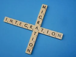 Auf einem blauen Untergrund liegen Holzsteinchen mit Buchstaben. Von oben nach unten ist das Wort „Migration“ gelegt, von rechts nach links das Wort „Integration“. Beide Wörter treffen sich am Buchstaben „A“.