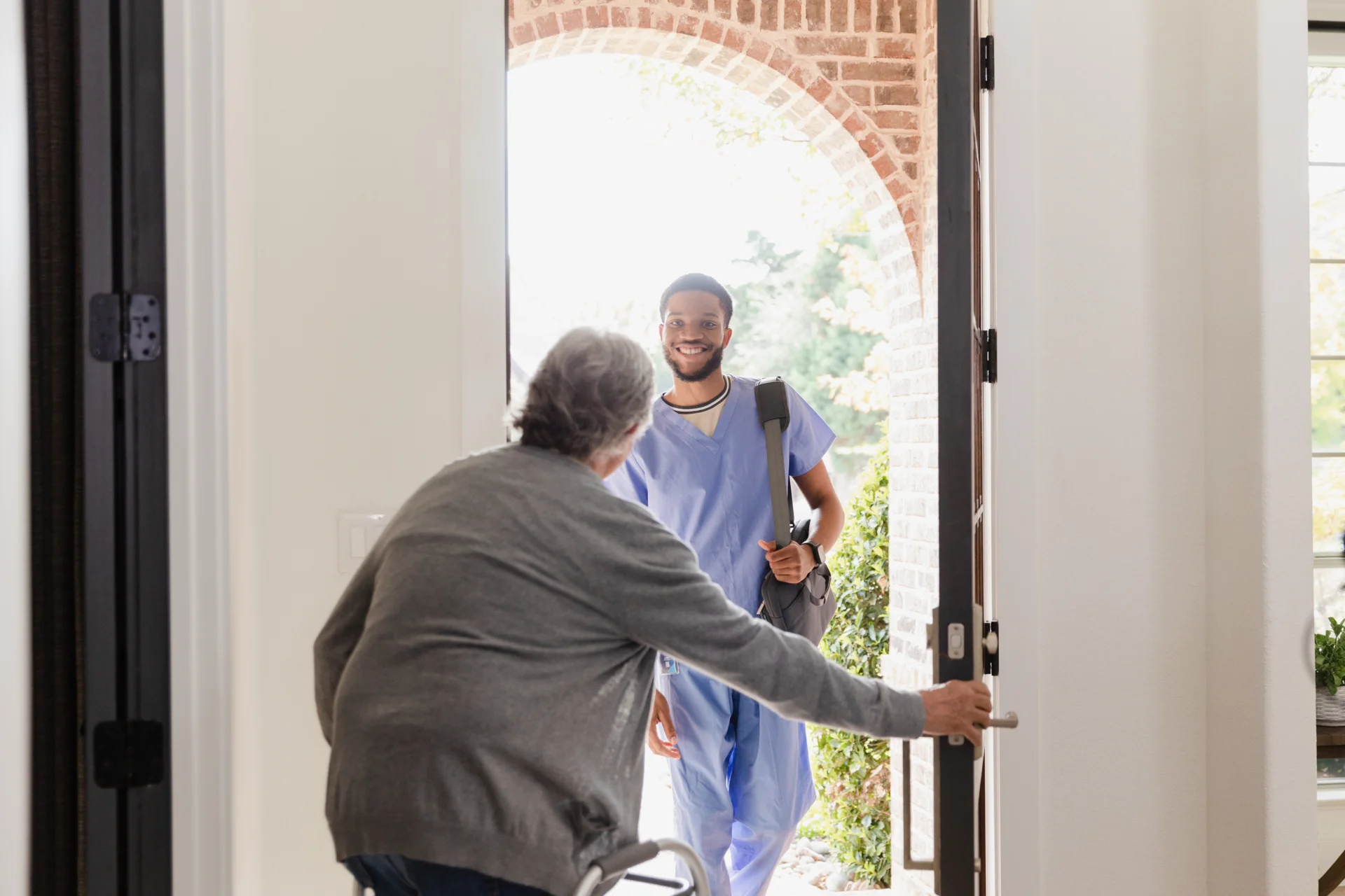 Senior-Mann mit Rollator öffnet Tür für Physiotherapeut