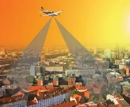 Kleines Flugzeug fliegt über Stadt mit Sonnenuntergang im Hintergrund und zwei sichtbaren Schattenstreifen auf den Gebäuden