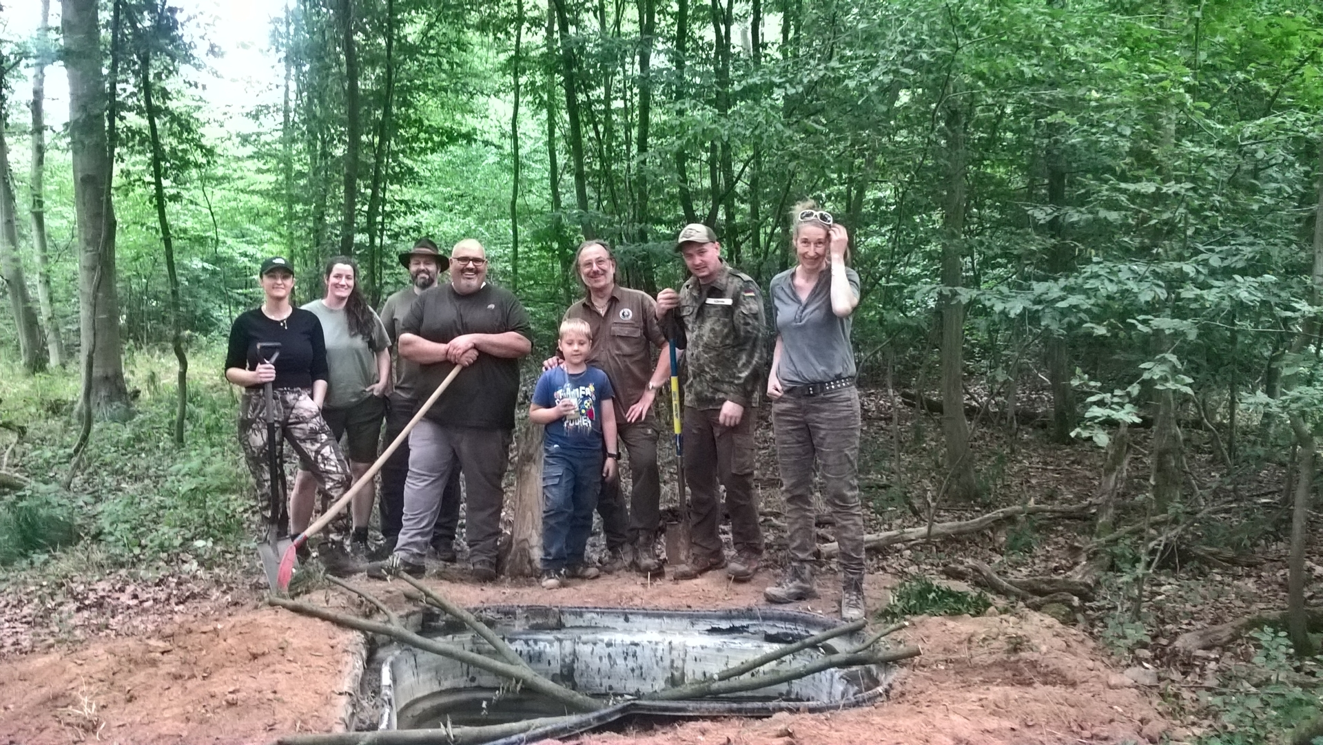 Jagdpächter Alfred Schneider und Freiwillige stehen vor einer Trinkwanne, die im Dörnigheimer Wald für Wildtiere eingegraben wurde.