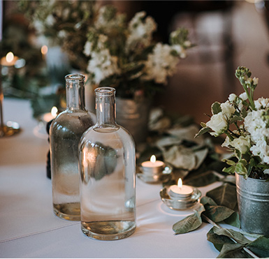 weisse-blumen-in-einem-eimer-wasserflaschen-und-kerzen-auf-einem-mit-blaettern-geschmueckten-tisch