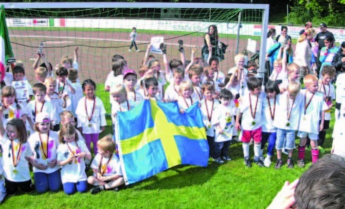 Kinder mit Medaillen feiern bei der Kindergarten-WM gemeinsam vor einem Fußballtor.