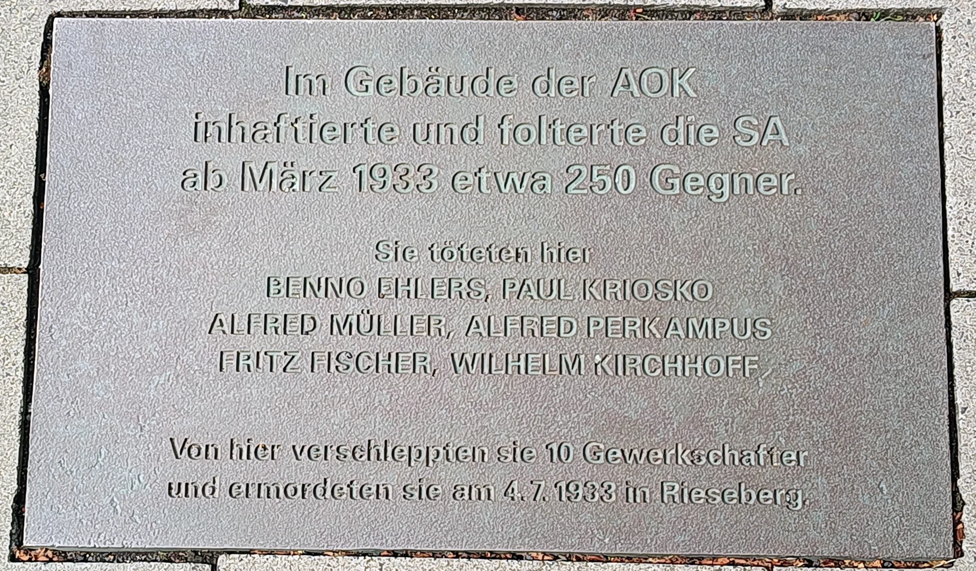 Abbildung 7: Gedenktafel am AOK-Gebäude in Braunschweig. Inschrift: "Im Gebäude der AOK inhaftierte und folterte die SA ab März 1933 etwa 250 Gegner. Sie töteten hier Benno Ehlers, Paul Kriosko, Alfred Müller, Alfred Perkampus, Fritz Fischer, Wilhelm Kirchhoff. Von hier verschleppten sie 10 Gewerkschafter und ermordeten sie am 4.7.1933 in Rieseberg.