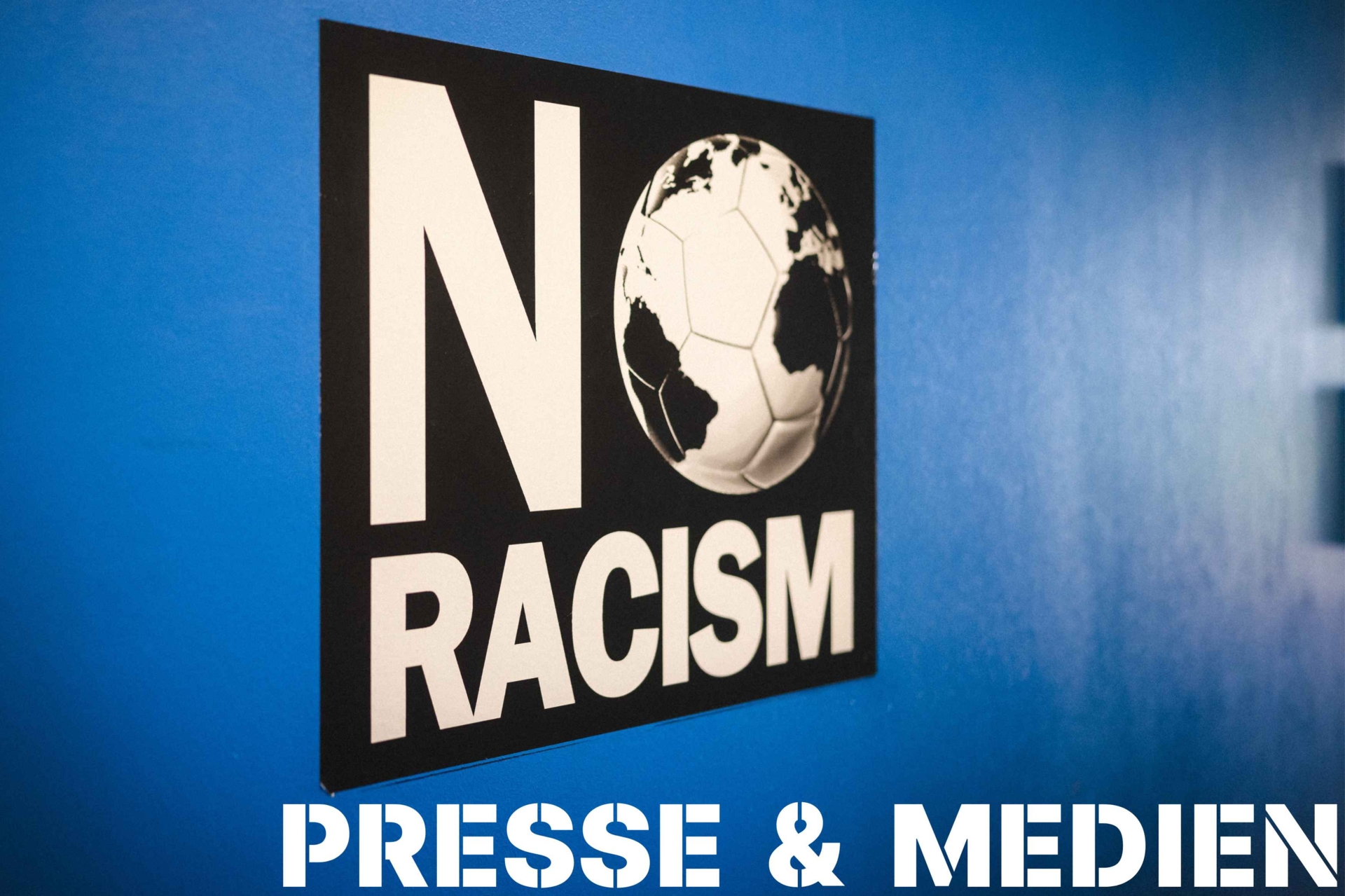Eine blaue Wand mit dem 'NO RACISM'-Logo darauf.