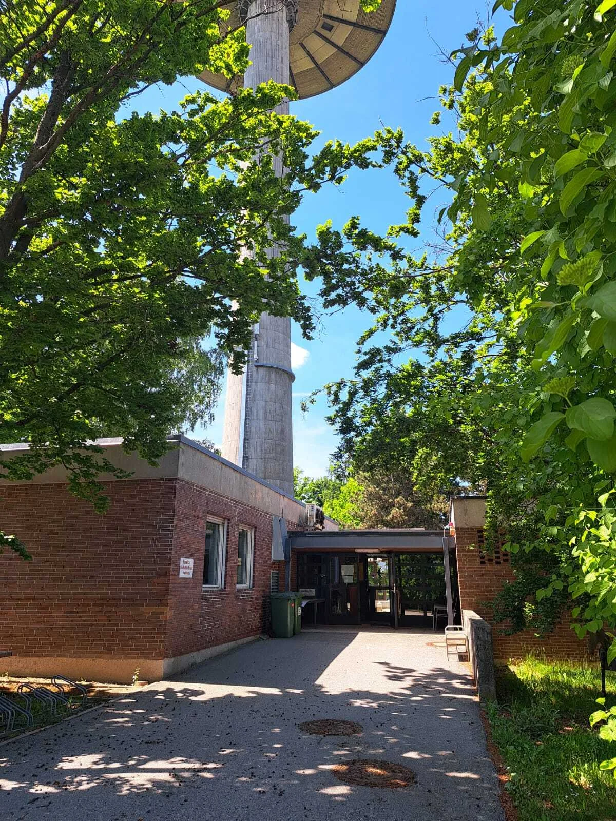 Zu sehen ist der Eingangsbereich der Geschäftsstelle des Stadtjugendring, ein rotes Backsteingebäude mit Bäumen im Vordergrund und dem Fernsehturm im Hintergrund.