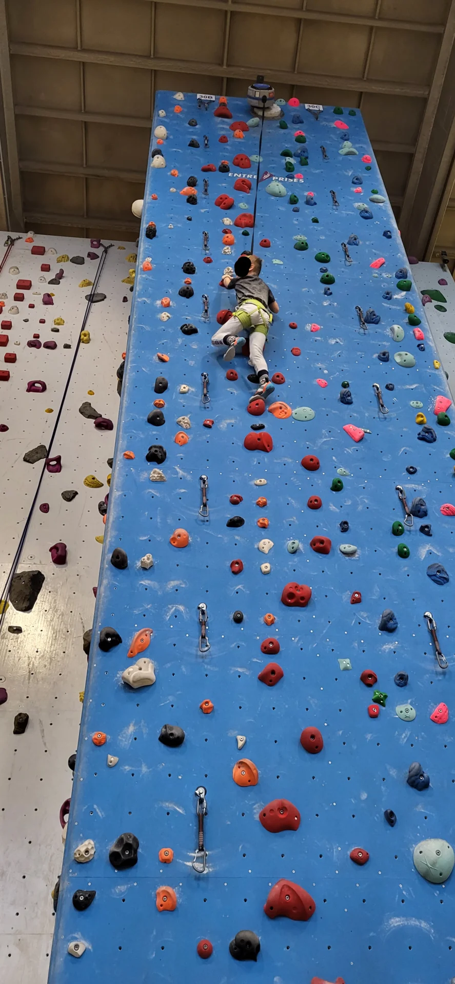 Kind klettert mit Sicherung an einer Wand hoch