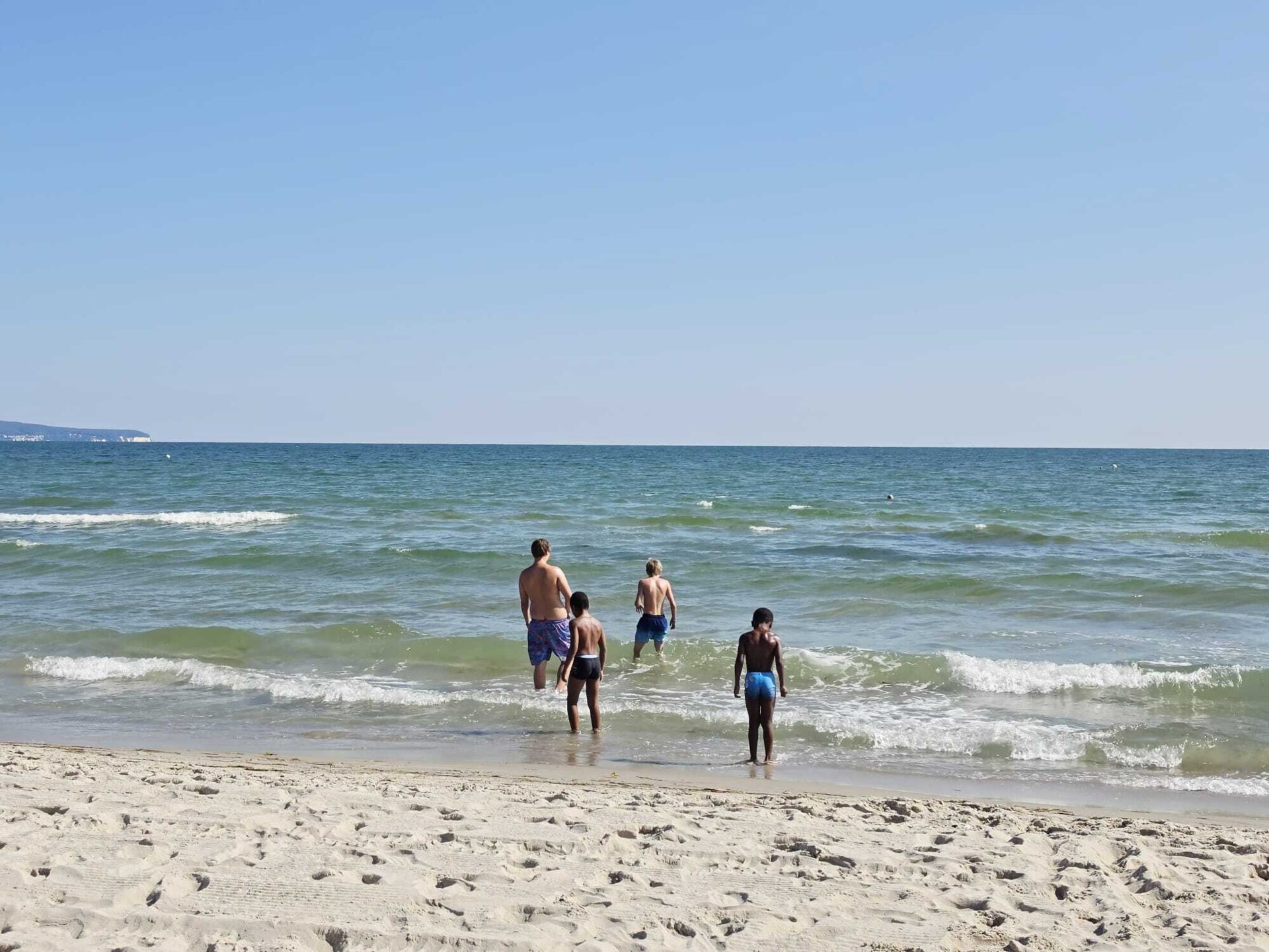 vier Kinder stehen im Meer mit dem Rücken zum Betrachter