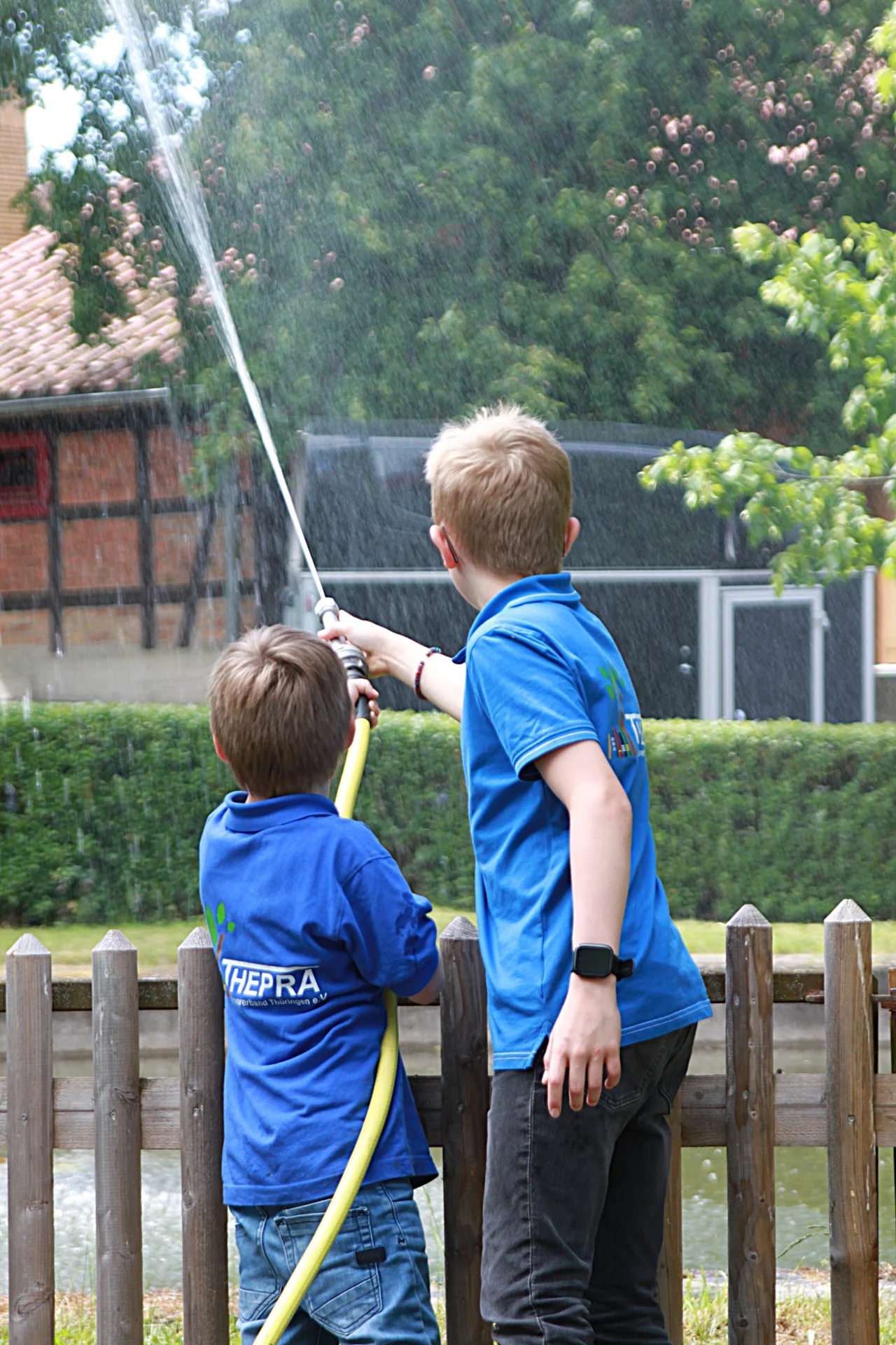 zwei Kinder spritzen mit einem Feuerwehr-Wasserschlauch in einen Teich