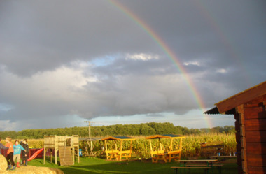 Sitzbereich des Maislabyrinths. Am Himmel ist ein Regenbogen zu sehen.